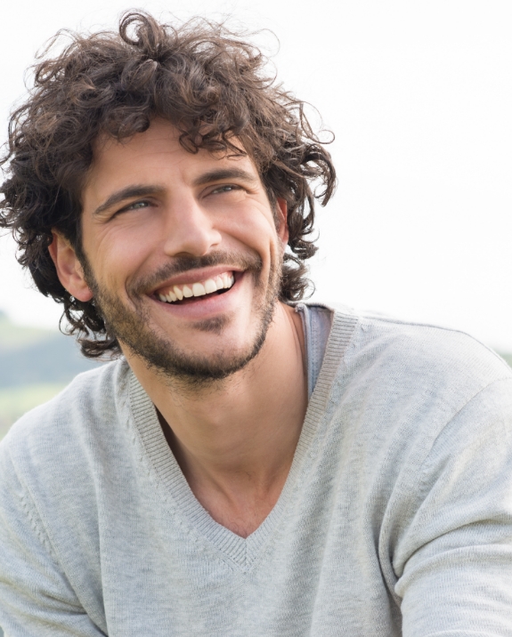 Young man with curly brown hair smiling outdoors