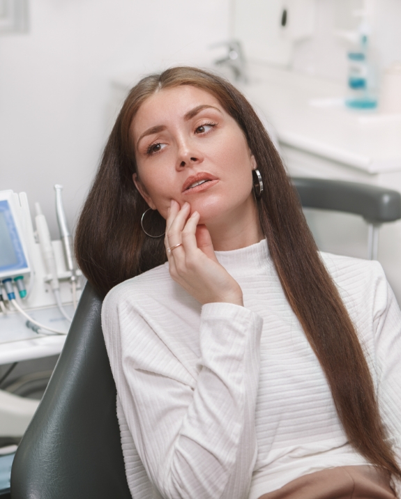 Wincing woman touching her cheek while visiting emergency dentist in Mesa