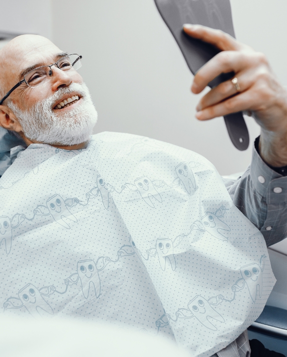 Senior man in dental chair admiring his smile in mirror