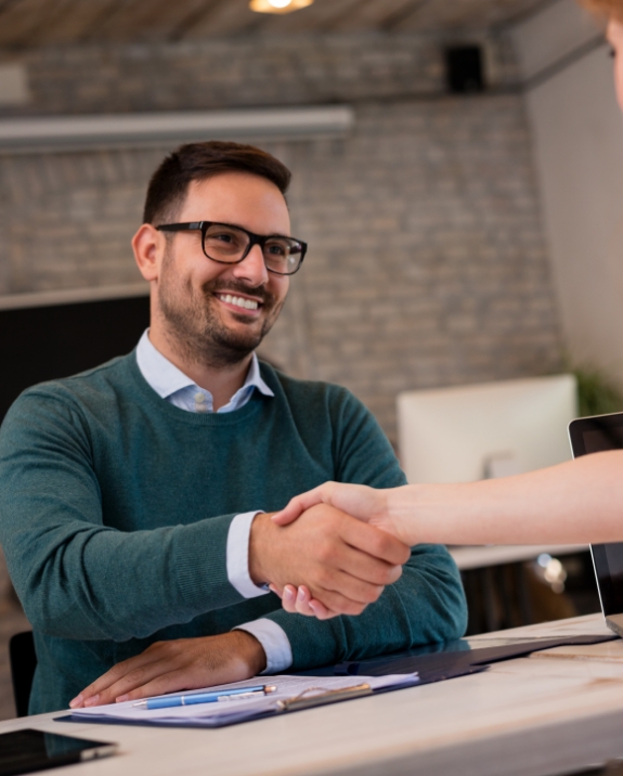 Smiling man shaking hands with person across desk