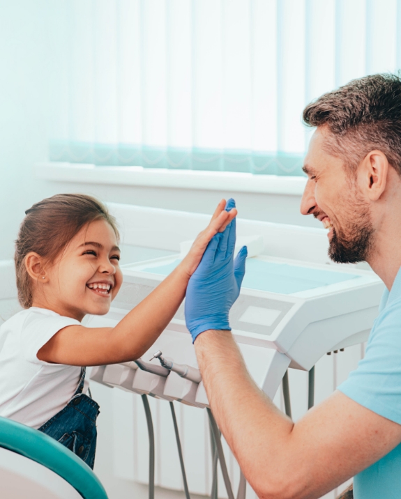 Young girl grinning and giving high five to her dentist