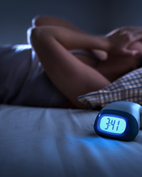 Woman lying awake in bed with clock on nightstand showing 3 41 A M