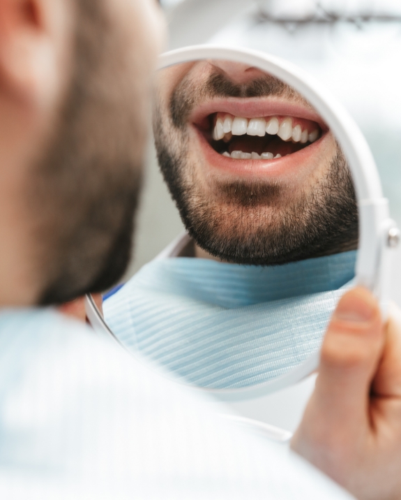 Man with short beard in dental chair admiring his smile in mirror 