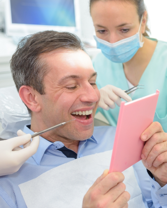 Man in dental chair looking at his smile in mirror