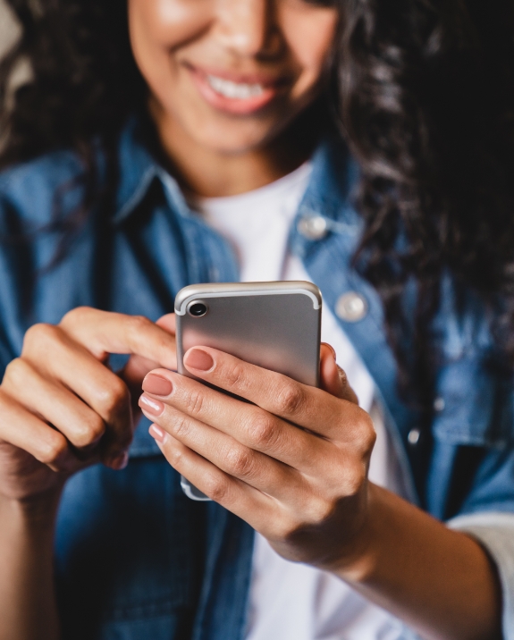 Smiling woman looking at her phone for dentist reviews in Mesa