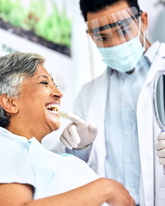 Dentist showing smiling patient reflection in handheld mirror