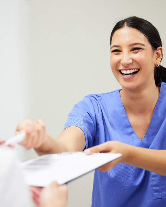 Dental assistant smiling while handing patient form