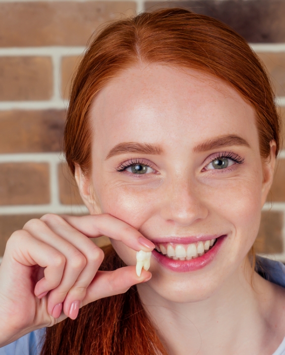 Smiling young woman holding an extracted wisdom tooth