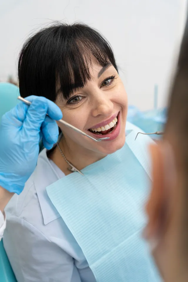 Dentist examining patient's teeth with tools; hands in gloves, mouth open, white backdrop.