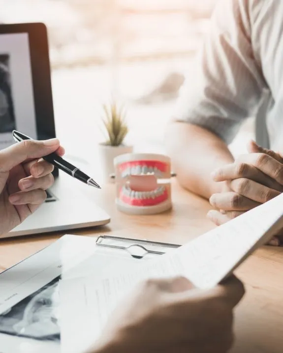 Dentist consults with patient, reviewing documents and dental model.