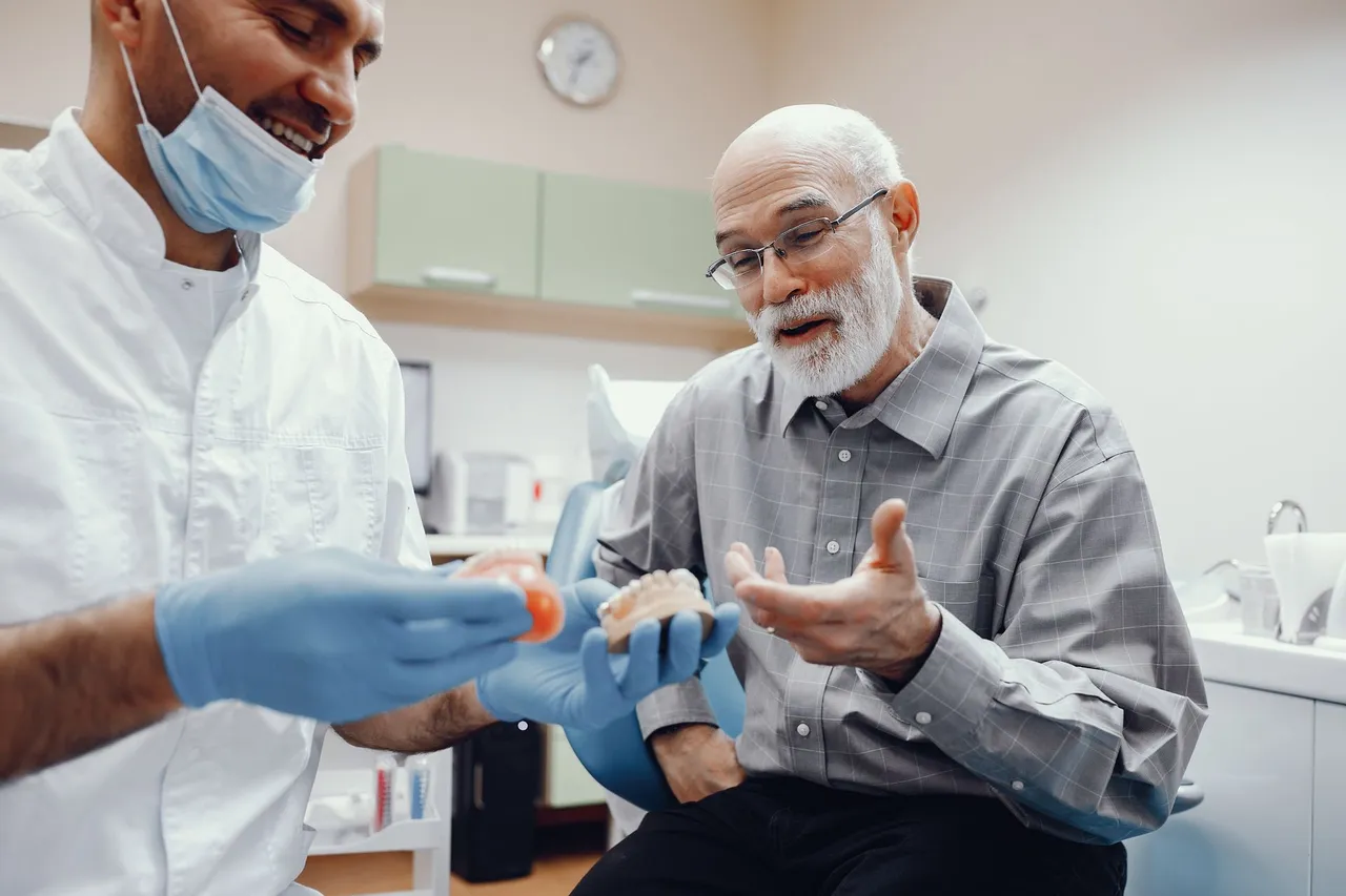 Dentist showing dentures to an older patient; both are smiling in a dental office.
