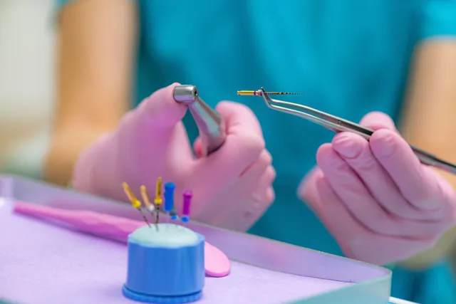 Dentist with gloved hands holding dental tools, preparing for a procedure.