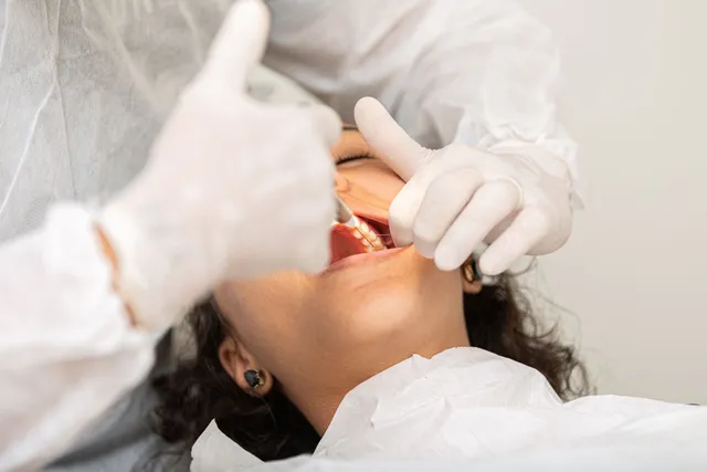 Dentist examining patient's mouth; both wear protective gear.