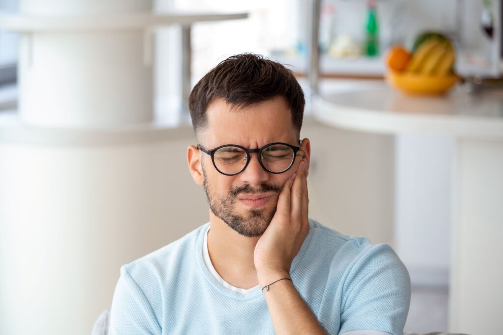 Man in glasses with eyes closed holding hand to jaw in pain